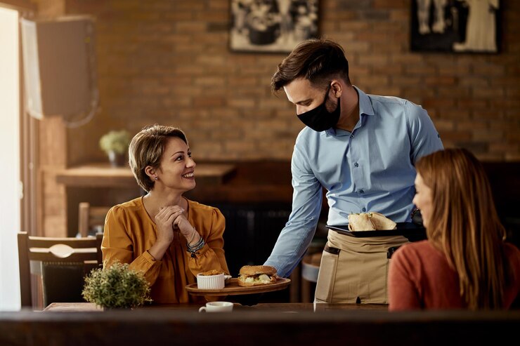 young-waiter-wearing-protective-face-mask-while-serving-food-his-guests-restaurant_637285-6633